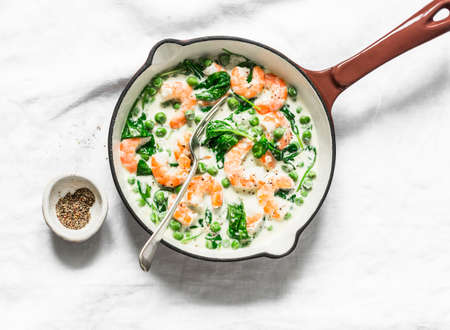 Seafood sauce for pasta. Fresh green peas, shrimps, spinach, cream sauce in a cast iron pan on a light background, top viewの写真素材