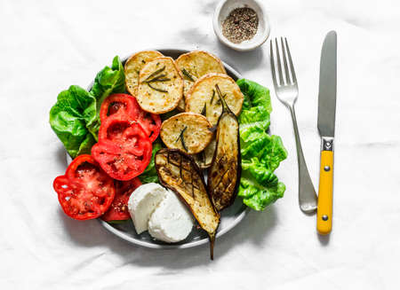 Vegetarian lunch, snack, tapas - rosemary roasted potatoes, grilled eggplant, tomatoes, green salad and greek cheese on a light background, top viewの写真素材