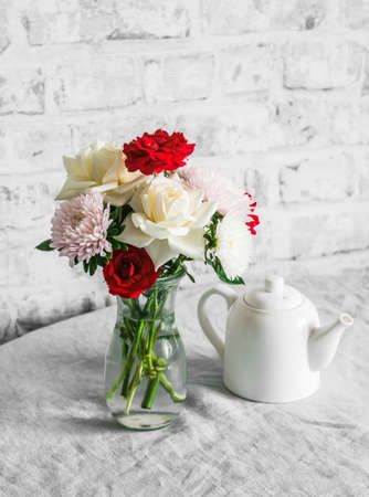 Bouquet of roses and asters in a glass vase, teapot on the table in a bright room. Cozy house interior still lifeの写真素材