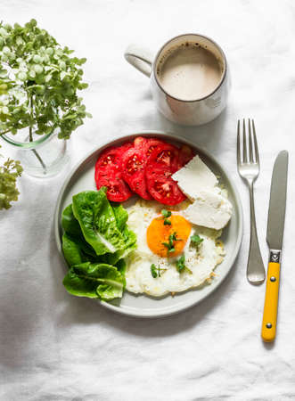 Delicious breakfast - fried egg, ripe tomatoes, greek cheese, green salad and coffee on a light background, top viewの写真素材