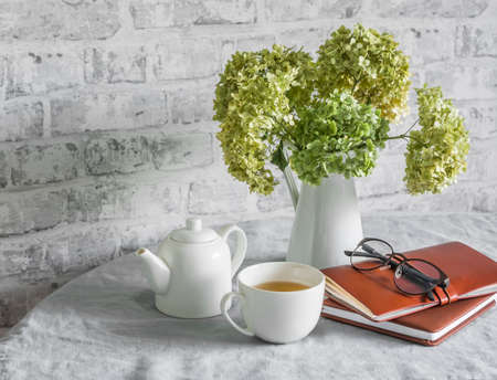 Morning planning day inspiration. Cup of green tea, leather organizer planner, bouquet of hydrangeas on the table in a bright roomの写真素材
