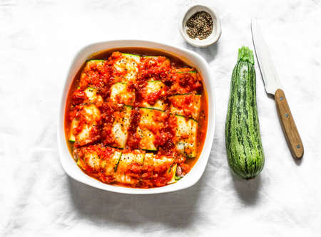 Cooking zucchini cannelloni with tomato sauce in a baking dish on a light background, top view. Raw food ingredientsの写真素材
