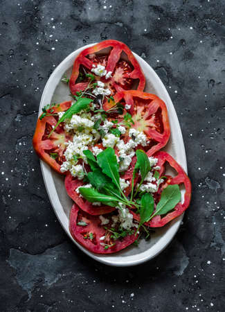 Fresh tomatoes, arugula, feta cheese appetizer on a dark background, top viewの写真素材