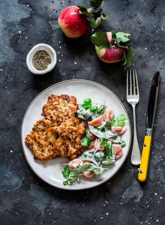 Delicious chicken breast, apple fritters and fresh tomatoes, cucumbers, arugula yogurt dressing salad on a dark background, top viewの写真素材