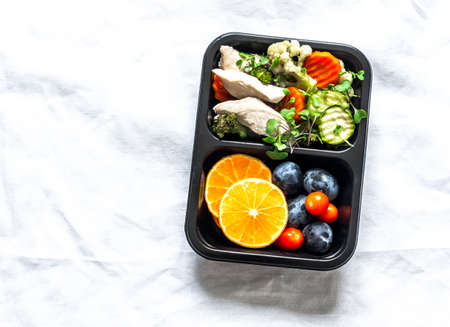 Healthy balanced lunch box - steamed vegetables and chicken breast and fresh fruit on a light background, top viewの写真素材