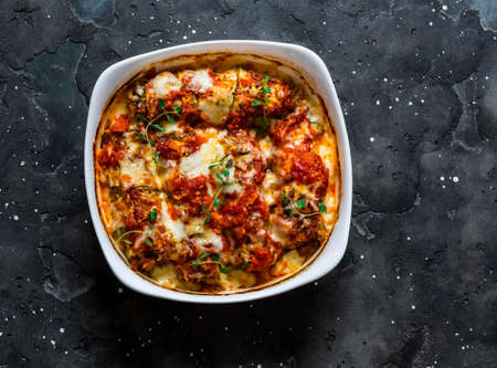 Zucchini cannelloni stuffed with meat with tomato sauce and mozzarella cheese on a dark background,...