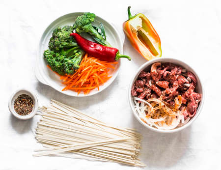 Asian style lunch cooking ingredients - beef in soy sauce, broccoli cabbage, carrots, peppers, udon noodles on a light background, top viewの写真素材