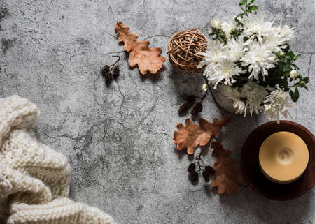 Cozy autumn background. Candle, autumn flowers, knitted blanket, dry leaves on a gray background, top viewの写真素材