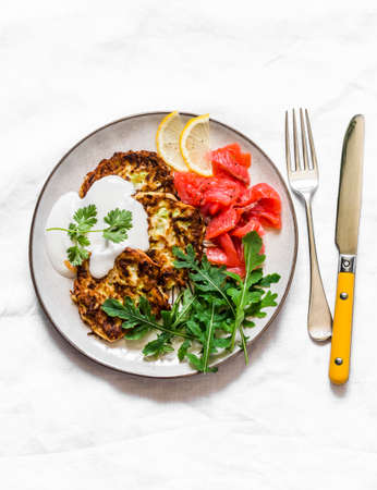 Zucchini and latkes with smoked salmon, sour cream and arugula. Delicious breakfast, brunch, tapas, appetizer on a light background, top viewの写真素材