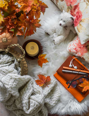 Basket with knitted blanket, bouquet of maple leaves, pillows, books, candle, toy bear on a fluffy carpet, top view. Cozy autumn house interior conceptの写真素材
