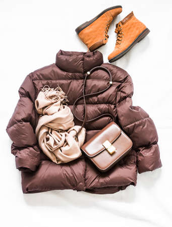 Women's down jacket, cashmere scarf, leather crossbody bag, oxford suede boots on a light background, top view. Autumn, winter women's clothing fashion conceptの写真素材