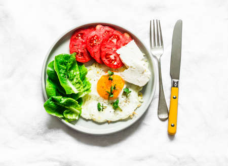 Breakfast, snack, tapas - fried egg, ripe red tomatoes, greek sheep cheese, green salad on a light background, top viewの写真素材
