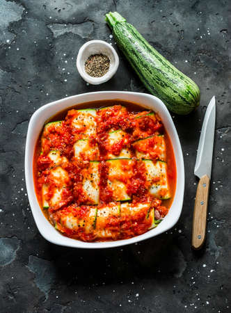 Preparing zucchini cannelloni with tomato sauce in a baking dish on a dark background, top view. Raw food ingredientsの写真素材