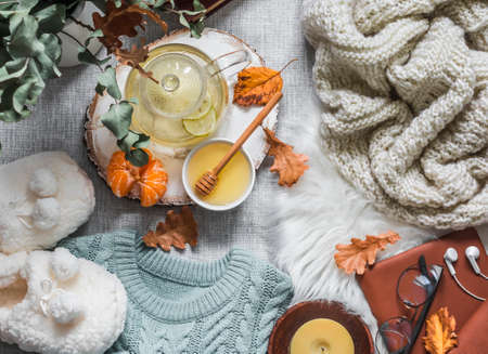Cozy home still life - soft slippers, knitted sweater, plaid, green tea with honey, tangerines, books on a light background, top view. Autumn and winter relaxing mood. Flat layの写真素材