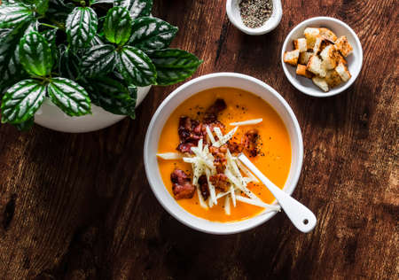 Pumpkin soup with crispy fried bacon and apple on a dark wooden background, top view