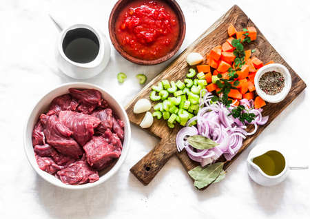 Ingredients for cooking beef in burgundy - beef fillet, tomato sauce, red wine, vegetables on a light background, top viewの写真素材