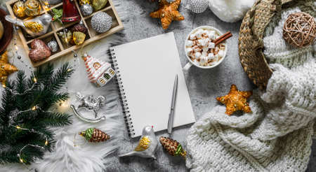 Christmas banner. Christmas coz background. Christmas planning notepad, toys, hot chocolate, basket with knitted blanket on a gray background, top viewの写真素材