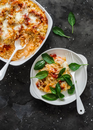 Roasted orzo pasta with tomato sauce and mozzarella cheese served with spinach on a dark background, top viewの写真素材
