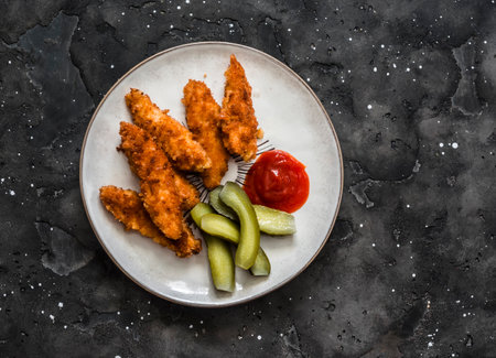 Chicken fingers, cornichons and ketchup - delicious tapas, appetizers, snack on the dark background, top viewの写真素材