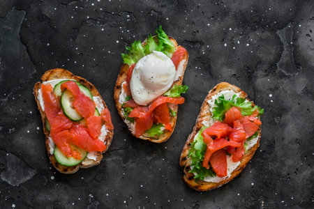Sandwiches with smoked salmon, green salad and boiled egg on the dark background. Delicious...