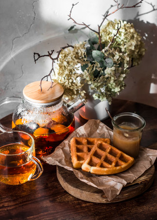 Viennese waffles, homemade apple sauce and fragrant citrus tea on a wooden table in a sunny and cozy roomの写真素材