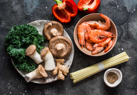 Cooking ingredients for asian style lunch - shrimp, egg noodles, variety of mushrooms, sweet pepper, kale on a dark background, top viewの写真素材