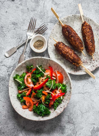Delicious lunch - kale, tomatoes, sweet pepper salad and kebabs on a gray background, top viewの写真素材