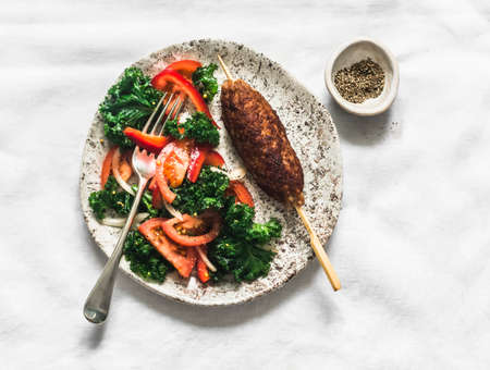 Fresh kale, tomatoes, bell pepper salad and meat kebab on a light background, top view
