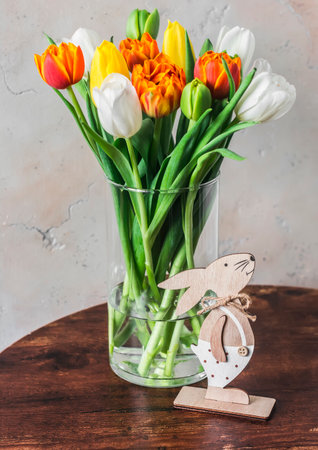 Easter still life. Bouquet of colorful tulips in a glass vase and a wooden Easter bunny decoration on the tableの写真素材