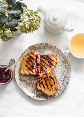 Delicious breakfast, snack - hot sandwiches with cranberry jam and camembert, green tea on a light background, top viewの写真素材