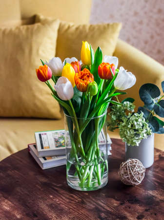 Cozy apartment interior-a bouquet of tulips in a vase, books on a wooden table on the background of a yellow sofaの写真素材