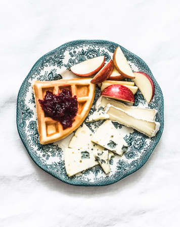 Delicious breakfast, snack - plate with waffle, cranberry jam, cheese and apple on a light background, top viewの写真素材