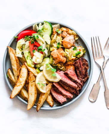 Barbecue cold cuts, potatoes and vegetable salad in a plate on a light background, top viewの写真素材