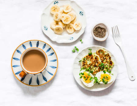 Delicious healthy breakfast - coffee with cream, zucchini latkes, boiled eggs, micro greens, banana...
