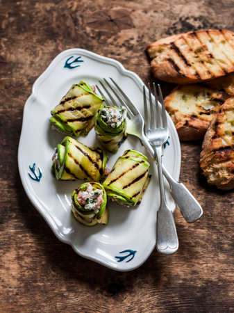 Delicious tapas, appetizer - grilled zucchini stuffed with cream cheese, smoked salmon and herbs on a wooden background, top viewの写真素材