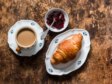 Croissant, coffee with cream, cranberry jam on a wooden background, top viewの写真素材