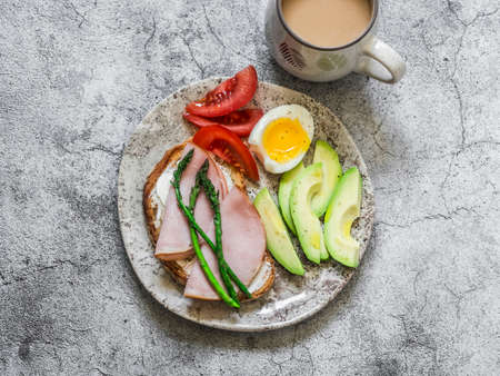 Delicious brunch, breakfast, snack - coffee, sandwich with cottage cheese, ham, asparagus, avocado, boiled egg, tomato on a gray background, top viewの写真素材