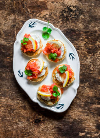 Delicious tapas, appetizer, breakfast - mini pancakes with salmon, cream cheese and lemon on a wooden background, top viewの写真素材