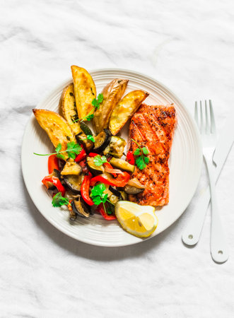 Healthy balanced lunch - grilled salmon, baked ratatouille and potatoes on a light background, top viewの写真素材