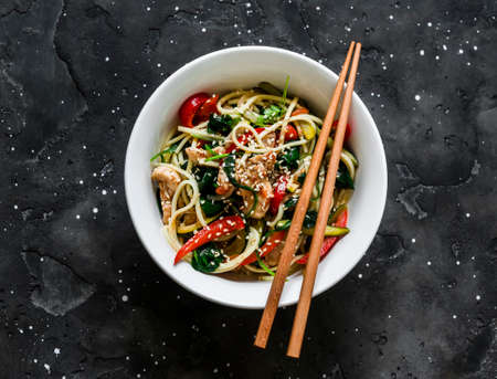 Stir fry vegetables zucchini, pepper, spinach and chicken with egg noodles on a dark background, top viewの写真素材