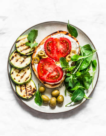 Sandwich with whipped ricotta, tomatoes, olives and grilled zucchini - delicious snack, tapas on a light background, top viewの写真素材