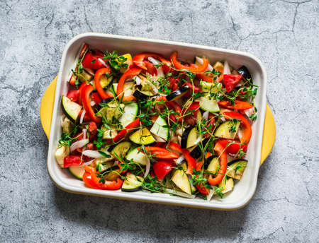 Raw ingredients for making roasted ratatouille. Vegetables - eggplant, zucchini, pepper, tomatoes, onion, garlic, rosemary, thyme cut in a baking dish on a gray background, top viewの写真素材