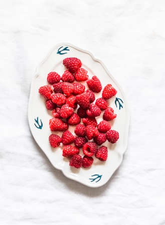 Fresh ripe raspberries on a vintage plate on a light background, top view
