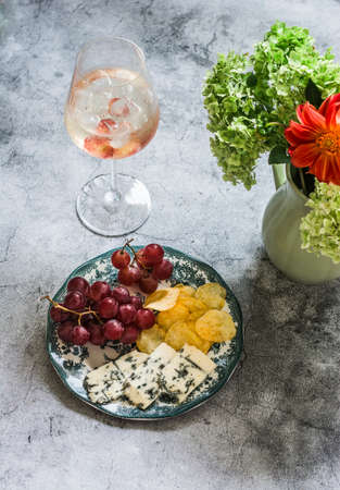 Aperitif - cocktail and a plate with grapes, cheese and chips on a gray background, top view