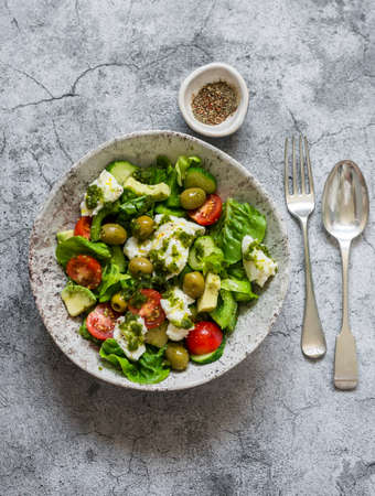 Fresh vegetable salad with tomatoes, avocado, lettuce, cucumbers, burrata and pesto sauce dressing on a gray background, top viewの写真素材