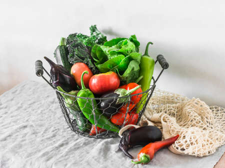 A basket with fresh vegetables. Organic harvest in a vintage metal basket - eggplant, kale, tomatoes, zucchini, pepper on a light background. The concept of healthy eatingの写真素材