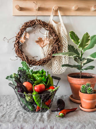 Cozy autumn still life in the hallway - a basket with seasonal vegetables, a ficus flower, a wreath of vines, a wooden shelf. House interior conceptの写真素材