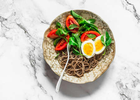 Asian-style breakfast - buckwheat noodles, boiled egg, tomatoes, spinach salad on a light background, top viewの写真素材