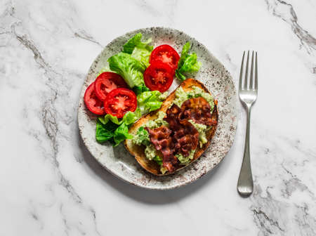 Delicious breakfast, brunch tapas - avocado, bacon sandwich and tomato lettuce salad on a light background, top viewの写真素材