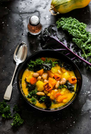 Pumpkin, potatoes, beans and kale stewed vegetarian autumn lunch on a dark background, top viewの写真素材